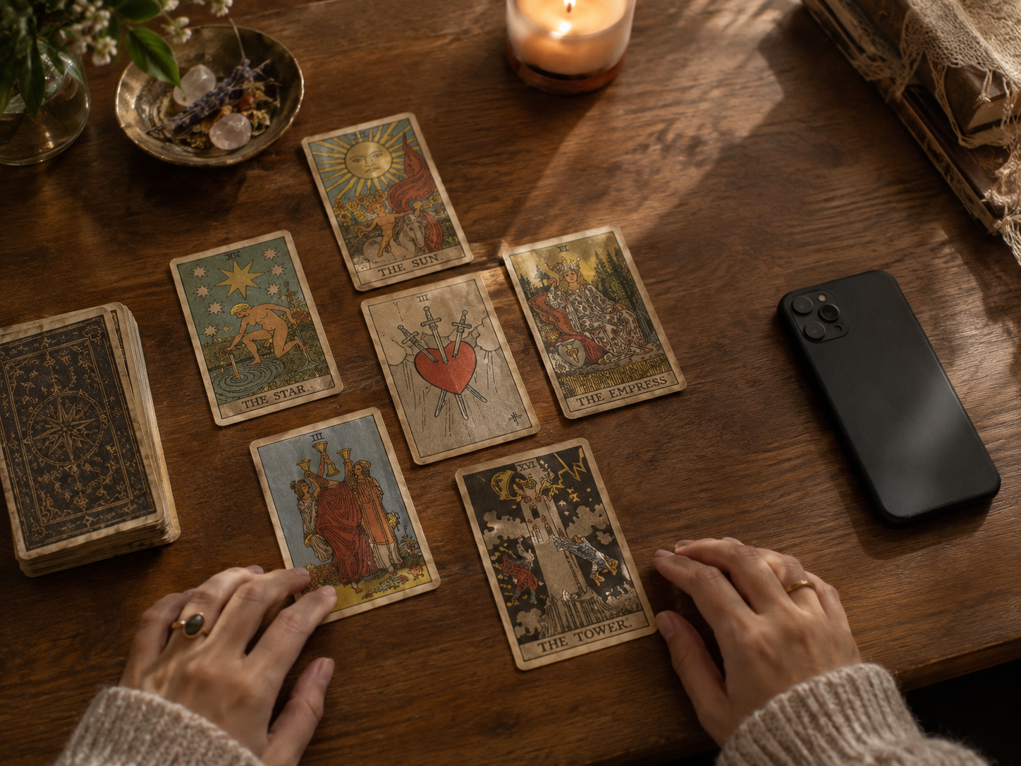 Hands resting near a spread of tarot cards and a phone on a table, showing the two ways to have a reading with Astara
